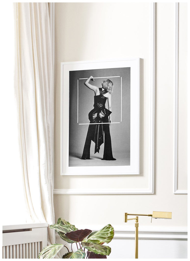 Also Magic Poster - Svart-vit fotokonst inramad hängandes i en vardagsrumsmiljö. Modefotografi, i en svart ram föreställande kvinna i studio som tycks hänga på en vit ram som svävar i luften.