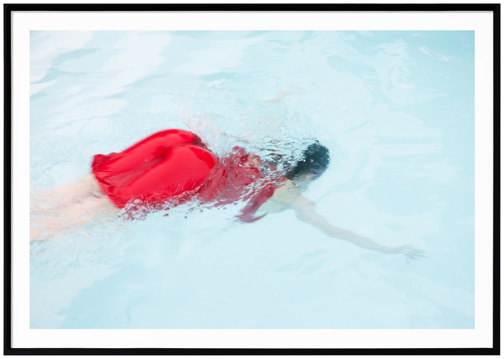 Poster av kvinna i röd klänning dykandes ner i ljusblå pool. Svart ram.