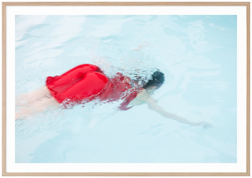 Poster av kvinna i röd klänning dykandes ner i ljusblå pool. Ekram.