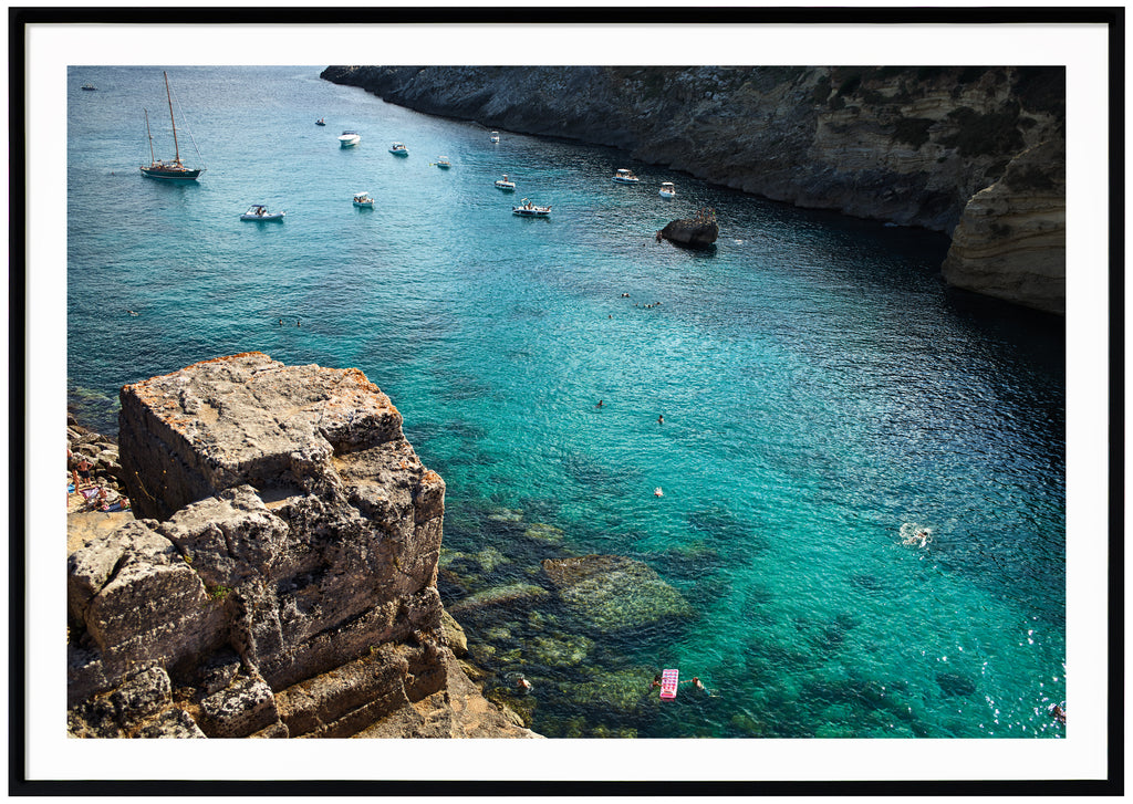Poster av klippor, vatten och båtar i södra Italien. Svart ram.