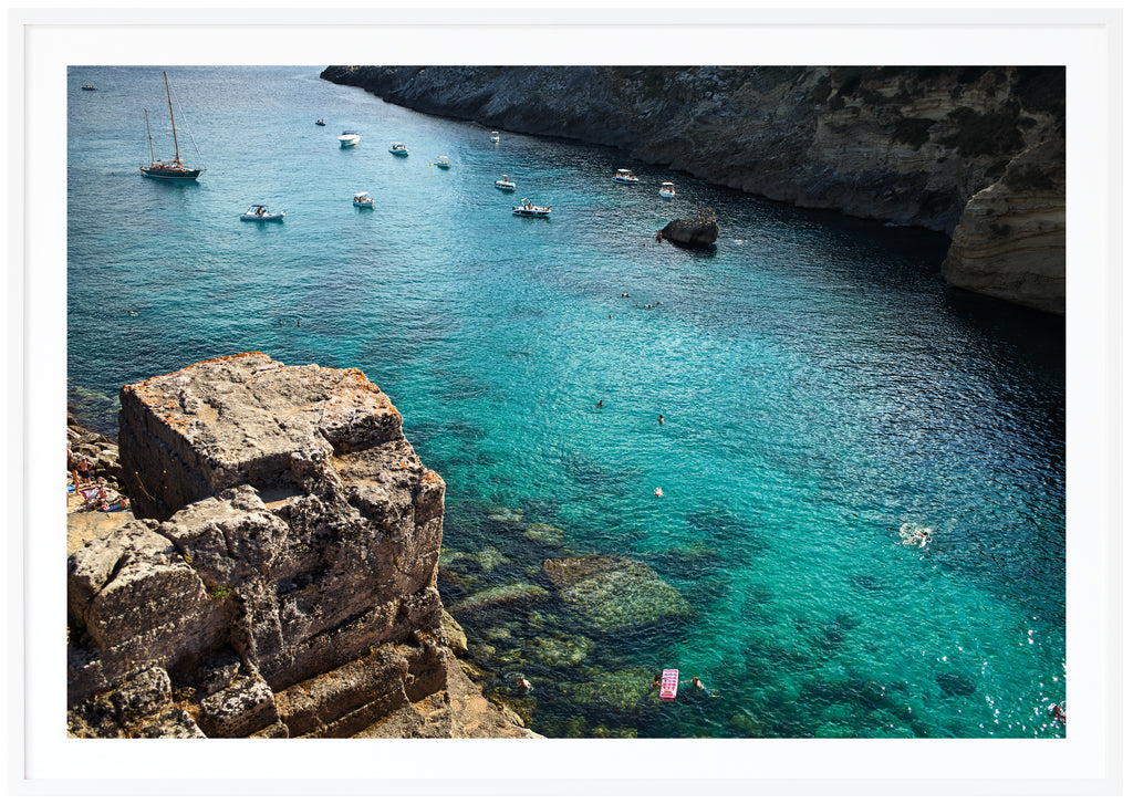 Poster av klippor, vatten och båtar i södra Italien.  Vit ram.