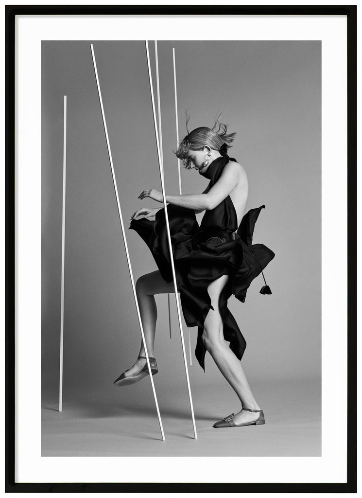 Svart-vit poster av kvinna klädd i svart sedd från sidan i fotostudio. Svart ram.