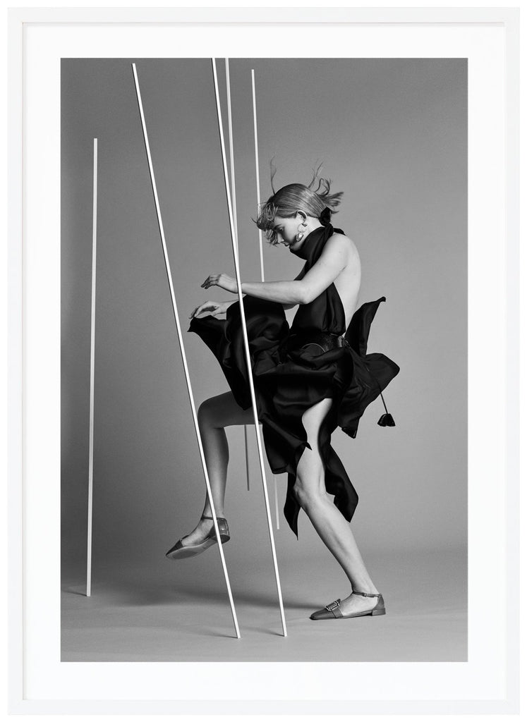 Svart-vit poster av kvinna klädd i svart sedd från sidan i fotostudio. Vit ram.