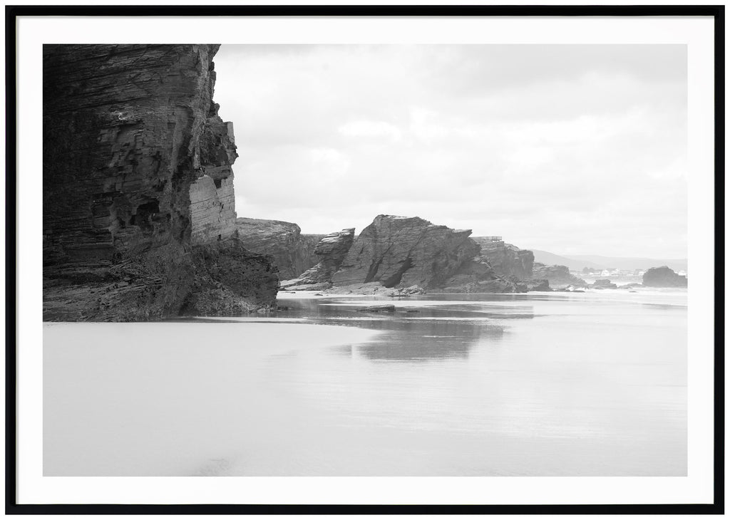Svart-vit poster av klippor vid strand. Svart ram.