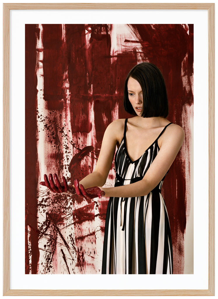 Poster av kvinna ståendes framför konstverk tittandes på sina händer. Ekram.