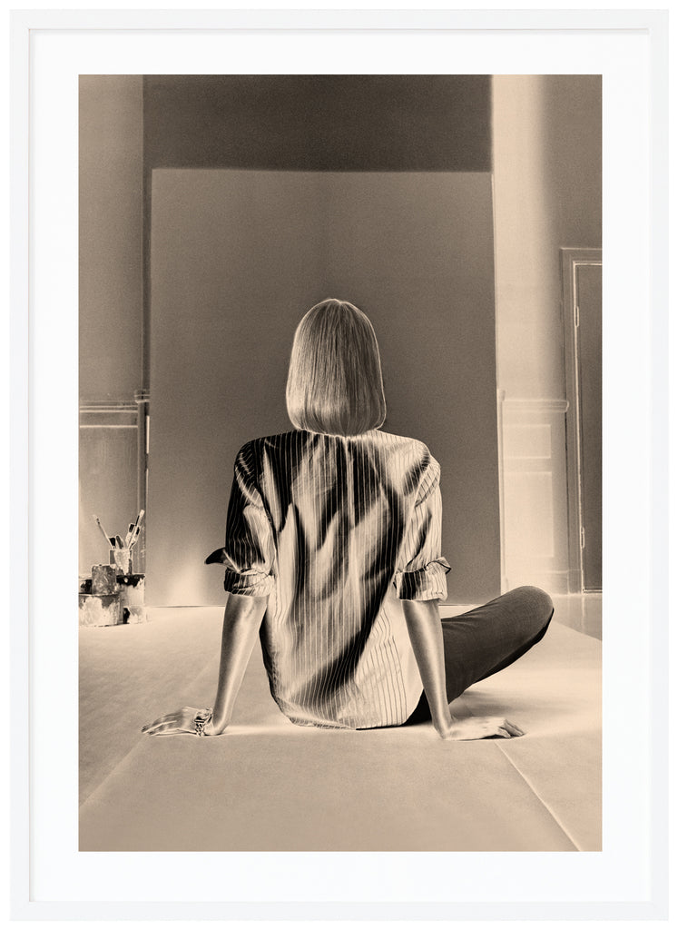 Svart-vit poster av en kvinna som sitter framför en tom kanvas. Vit ram.
