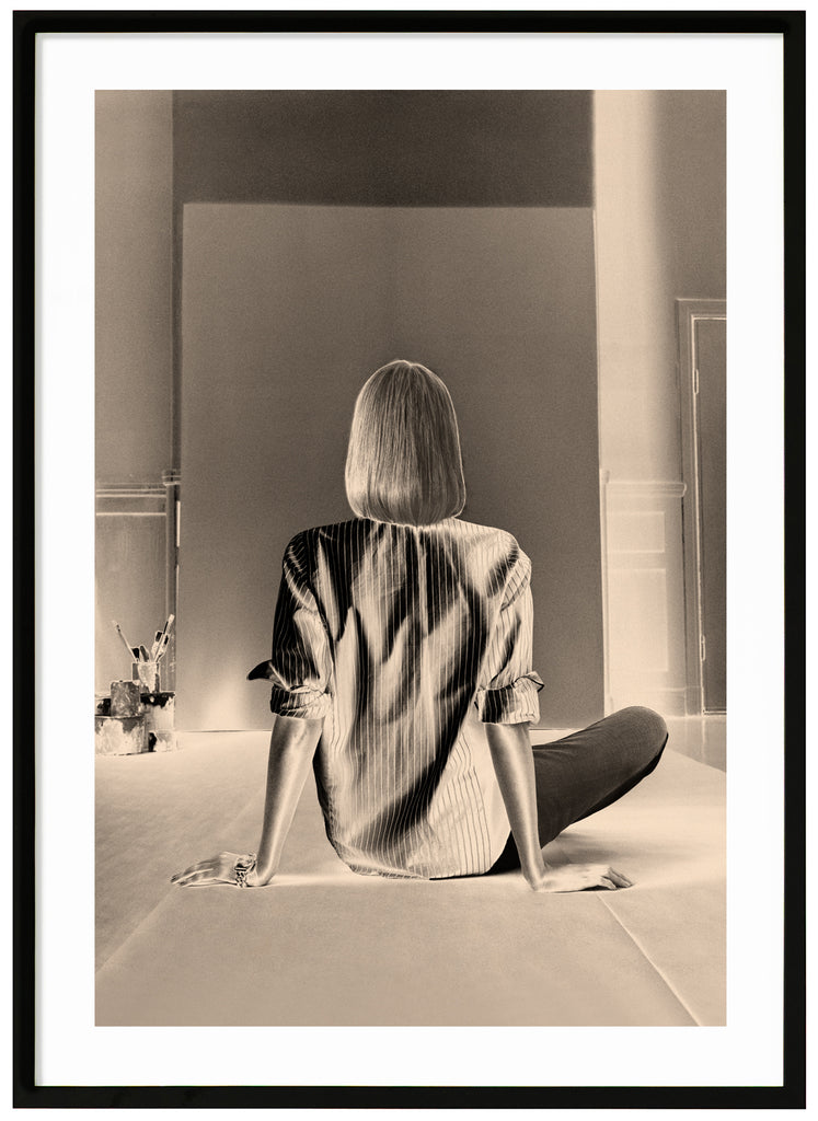 Svart-vit poster av en kvinna som sitter framför en tom kanvas. Svart ram.