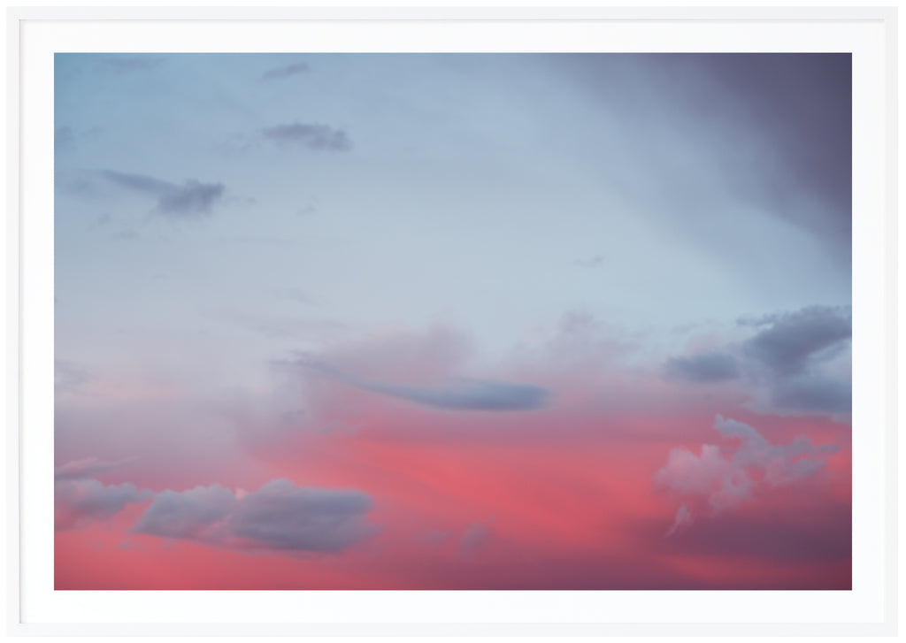 Poster av moln i rosa och blått sken. Liggande format. Vit ram.