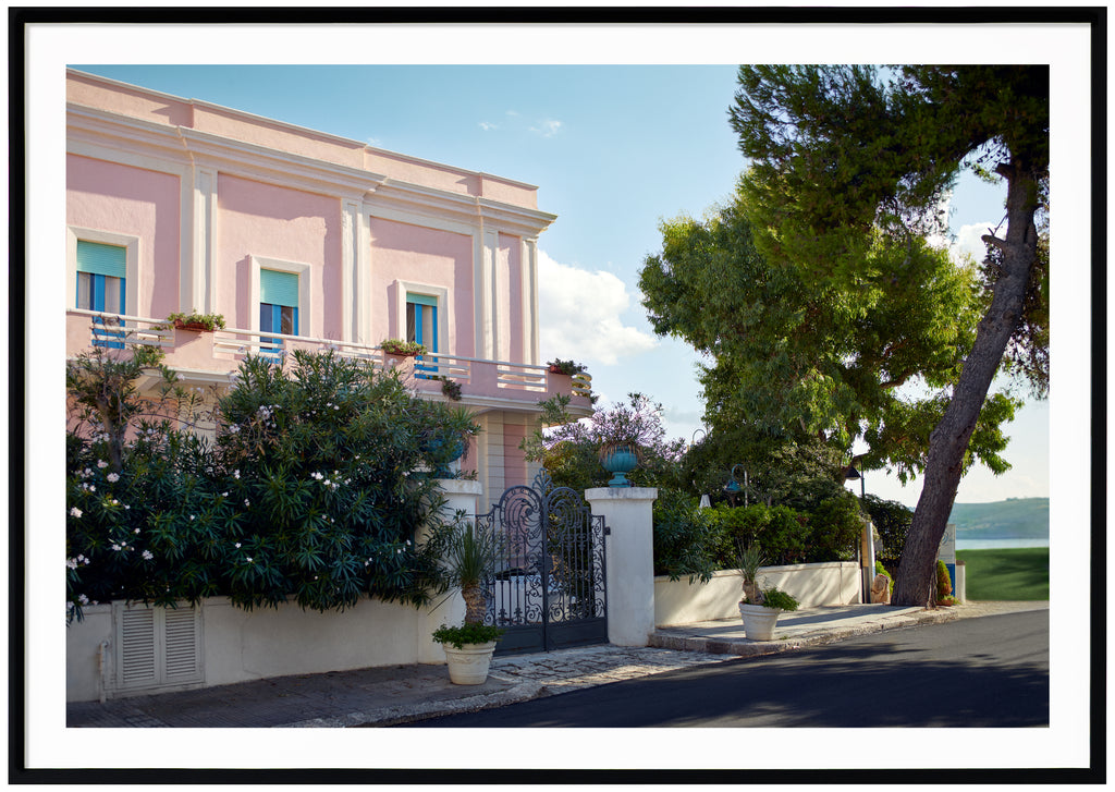 Poster av ett rosa hus med blå fönsterkarmar och turkosa luckor. Svart ram.