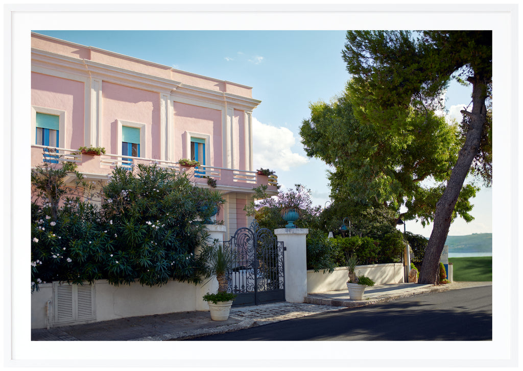 Poster av ett rosa hus med blå fönsterkarmar och turkosa luckor. Vit ram.