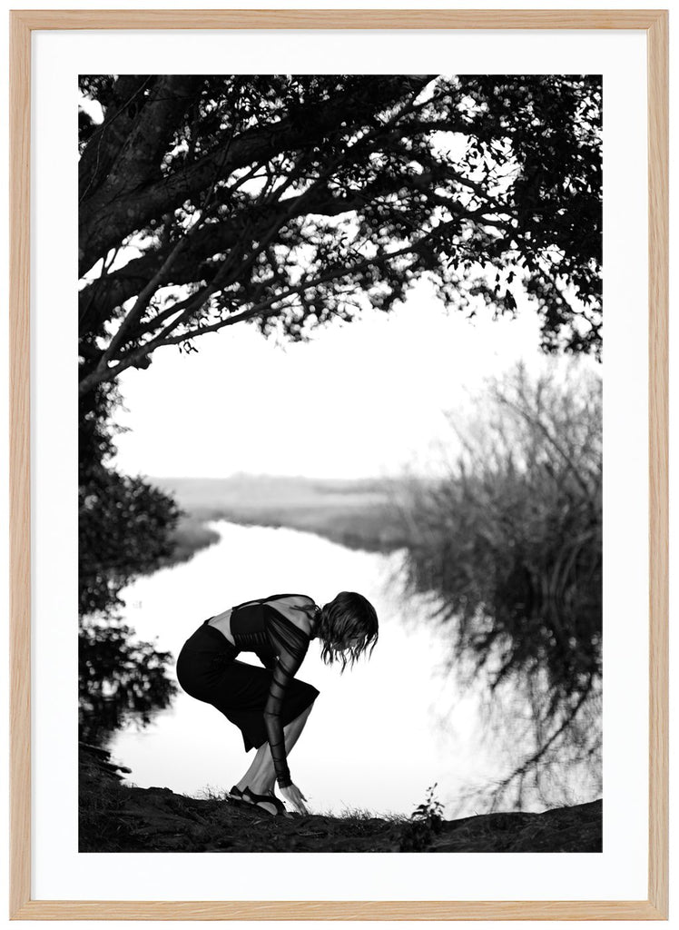 Poster av en kvinna som böjer sig vid vatten. Ekram.