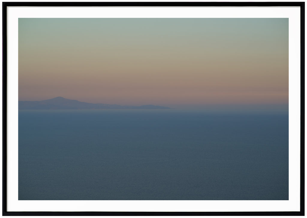 Poster av medelhavet vid Amalfikusten. Berg långt ut i havet och svaga färger i blå gul orange och rosa. Svart ram.