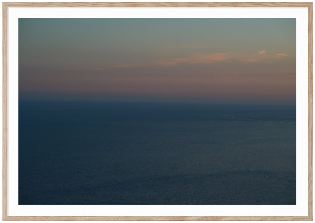 Poster av medelhavet vid Amalfikusten. Himlen är ljusblå orange och rosa i ljusa toner. Havet är blått. Liggande format. Ekram