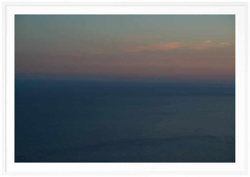 Poster av medelhavet vid Amalfikusten. Himlen är ljusblå orange och rosa i ljusa toner. Havet är blått. Liggande format. Vit ram
