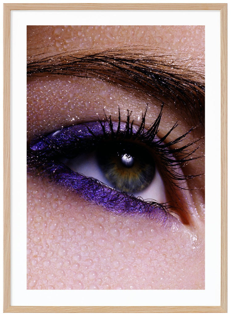 Poster av närbild på öga och ögonbryn med lila smink och vattendroppar över huden. Ekram.