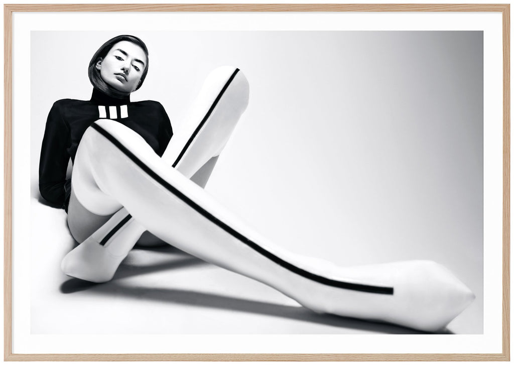 Svart-vit poster av kvinna sittandes på golvet. Vita overknee klackar med svart rand. Svart tröja. Liggande format. Ekram.