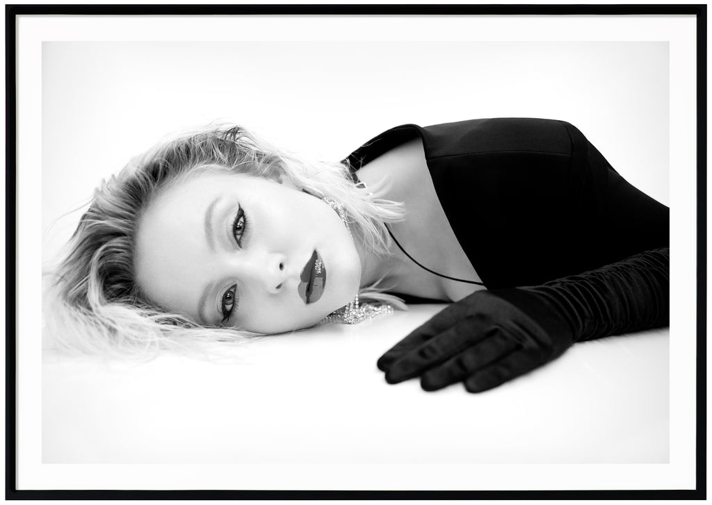 Svart-vit poster av Zara Larsson liggandes på mage med handskar. Svart ram.