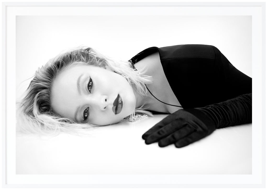 Svart-vit poster av Zara Larsson liggandes på mage med handskar. Vit ram.