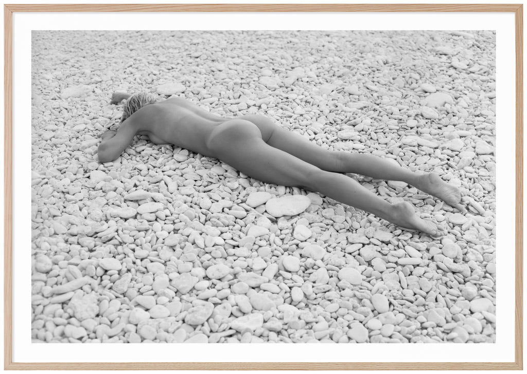 Svart-vit poster av kvinna liggandes på mage på strand med vita stenar. Liggande format. Ekram.