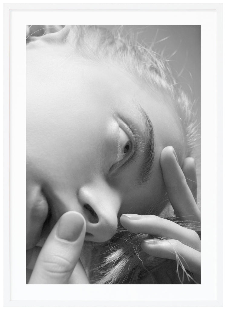 Svart-vit poster av kvinnas ansikte. Fotot är taget underifrån. Tumme som täcker munnen. Stående format. Vit ram.