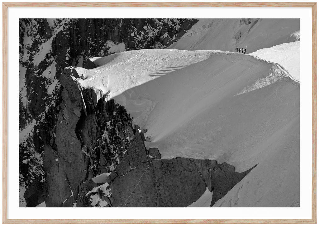 Svart-vitt fotografi av fyra skidåkare som vandrar på snötäckt bergskam. Ekram