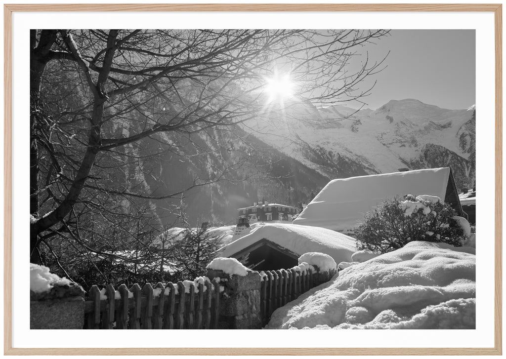 Svart-vitt fotografi av snötäckta hustak med alper i bakgrunden. Ekram