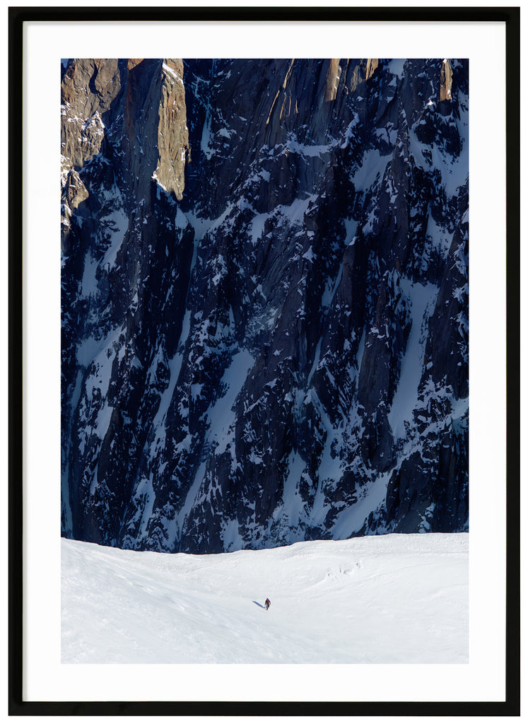 Färgfotografi av ensam bergsklättrare med branta klippor i bakgrunden. Svart ram