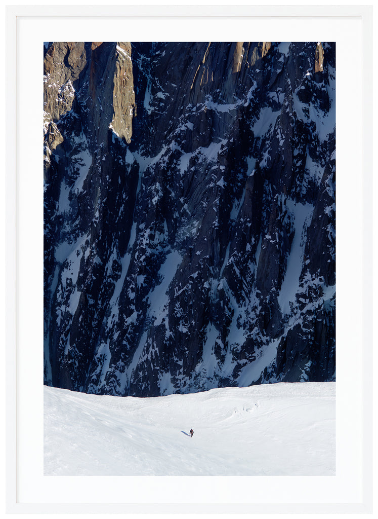 Färgfotografi av ensam bergsklättrare med branta klippor i bakgrunden. Vit ram