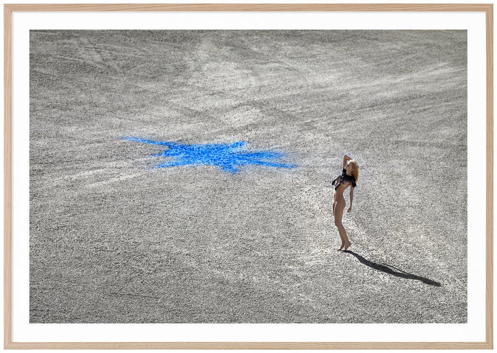 Poster i liggande format av naken kvinna ståendes på stenmark med en blå figur på. Ekram.