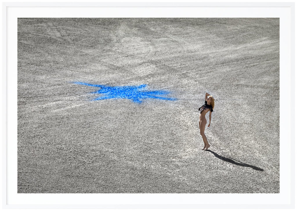 Poster i liggande format av naken kvinna ståendes på stenmark med en blå figur på. Vit ram.