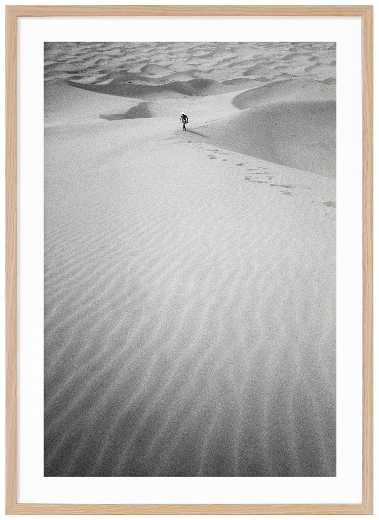 Svart-vitt analogt fotografi av en man på långt håll, som vandrar uppför en enorm sanddyna mitt i Saharaöknen. Ekram.