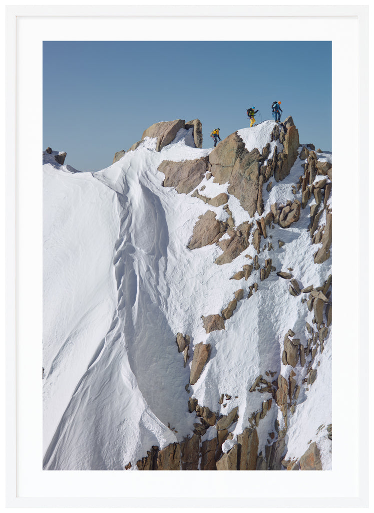 Färgfotografi av tre bergsklättrare på toppen av branta klippor. Vit ram.