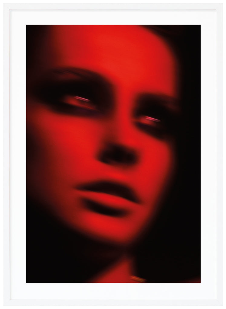 Fotografi i tonerna röd och svart, av en kvinna i svart smink runt ögonen. Vit ram. 