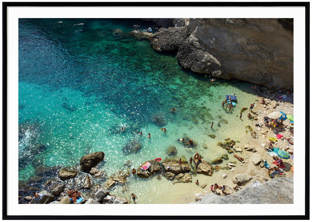 Fotografi i färg av en strand och klippor i södra Italien. Svart ram. 