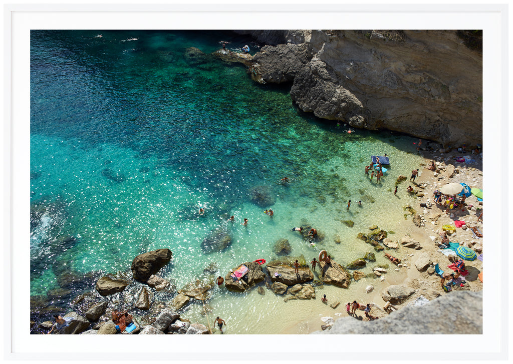Fotografi i färg av en strand och klippor i södra Italien. Vit ram. 