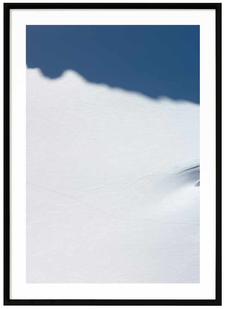 Färgfotografi av enorm snötäckt yta med två skidåkare som knappt syns. Svart ram.  