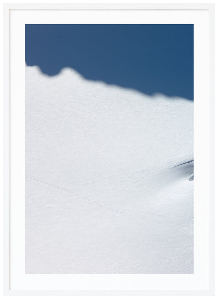 Färgfotografi av enorm snötäckt yta med två skidåkare som knappt syns. Vit ram.