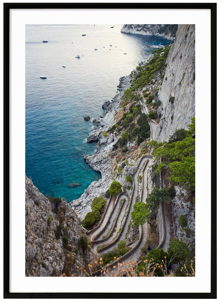 Fotografi i färg av utsikt över ett promenadstråk i sten på Italienska ön Capri. Verticale. Svart ram.